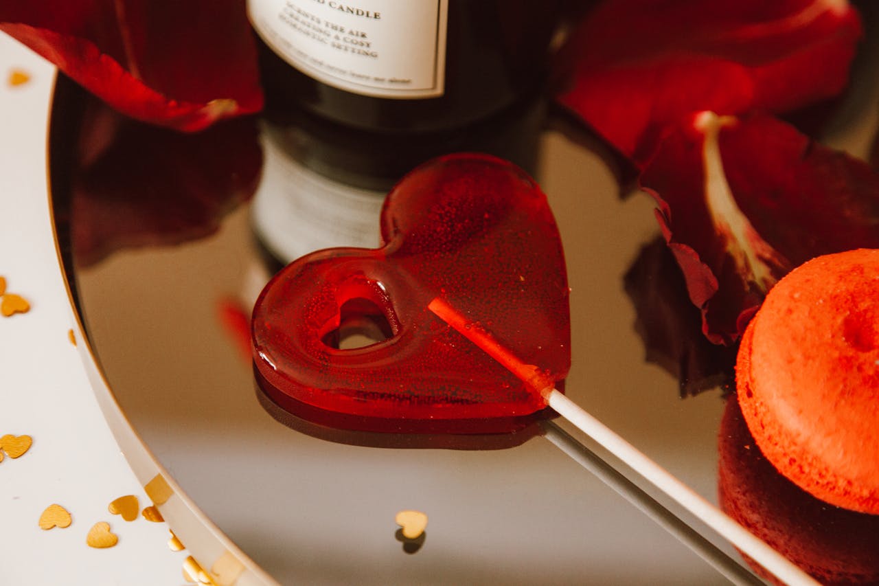 Heart-shaped red lollipop with rose petals and gold hearts, perfect for Valentines Day themes.